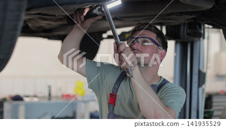 Auto mechanic working underneath car lifting machine at the garage. Car auto service. Auto mechanic working underneath car lifting machine at the garage. Car auto service. 141935529