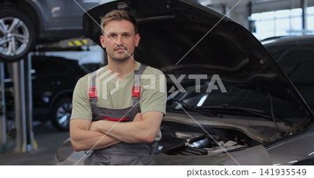 Portrait of a skilled car mechanic in a workshop, with service in the background. Portrait of a skilled car mechanic in a workshop, with service in the background. 141935549