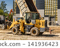 A yellow loader is working on a construction site. It is lifting soil and unloading it at the base of a new structure being built 141936423