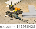 Several construction tools and materials are on the ground at a building site. There are power tools, cables, and safety gear ready for use 141936428
