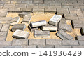 Bricks lay scattered on sand in a gap of a paved surface. Nearby, the surrounding bricks align neatly. This scene takes place during a construction project 141936429