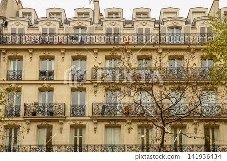 Typical Parisian architecture with multiple floors, intricate ironwork balconies, and traditional dormers against a clear sky Typical Parisian architecture with multiple floors, intricate ironwork balconies, and traditional dormers against a clear sky 141936434
