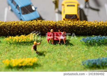 Miniature park scene with seated figures waving beside blurred toy cars Miniature park scene with seated figures waving beside blurred toy cars 141936492