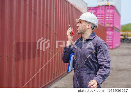 Warehouse worker using walkie-talkie for communication at shipping yard. Warehouse worker using walkie-talkie for communication at shipping yard. 141936917