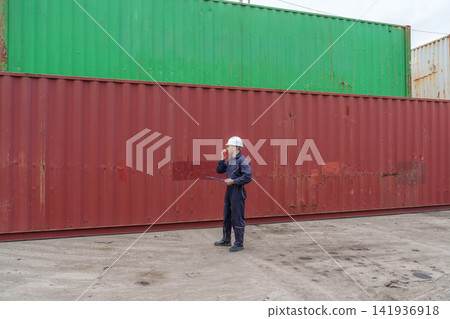 Construction worker inspecting cargo containers at shipping yard. Construction worker inspecting cargo containers at shipping yard. 141936918