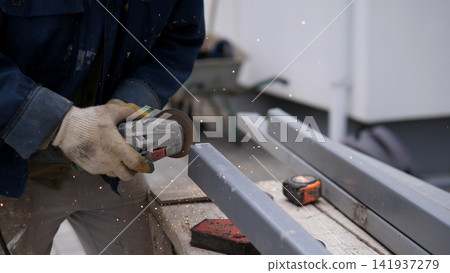 Worker grinding metal, in construction site, with angle grinder, metal beam, measuring tape, from a close-up perspective, with gray, blue accents, and focused mood, nearby objects. Worker grinding metal, in construction site, with angle grinder, metal beam, measuring tape, from a close-up perspective, with gray, blue accents, and focused mood, nearby objects. 141937279