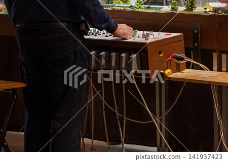 Man operating a wired control console beside an indoor model railway Man operating a wired control console beside an indoor model railway 141937423