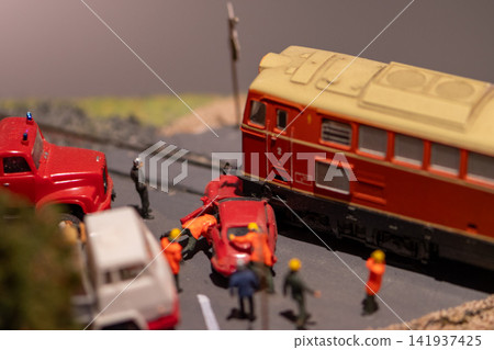 Miniature train collision scene with emergency workers around crushed red car 141937425