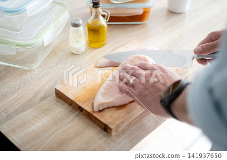 Man Cutting Raw Chicken Breast in Home Kitchen Man Cutting Raw Chicken Breast in Home Kitchen 141937650