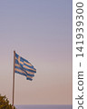 Tattered Greek national flag waving in strong wind on flagpole against clear sky and sea horizon close up Greek symbol travel stock photo 141939300