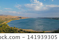 Aerial panoramic view of Tbilisi Reservoir sea with blue water surrounded by hills pine forest and distant sailboats under sunny cloudy sky in Georgia stock photo 141939305