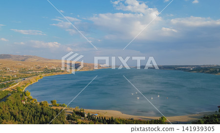 Aerial panoramic view of Tbilisi Reservoir sea with blue water surrounded by hills pine forest and distant sailboats under sunny cloudy sky in Georgia stock photo Aerial panoramic view of Tbilisi Reservoir sea with blue water surrounded by hills pine forest and distant sailboats under sunny cloudy sky in Georgia stock photo 141939305