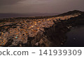 Aerial wide view of illuminated Oia village on cliff top at night dusk on Santorini island Aegean sea Greece Mediterranean coastal town cityscape lights photo 141939309