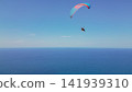 Paraglider with motor flying with colorful wing over deep blue sea water under clear sky extreme sport freedom leisure activity stock photo 141939310