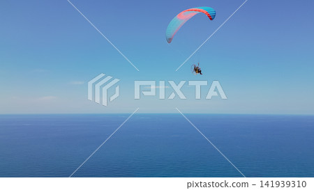 Paraglider with motor flying with colorful wing over deep blue sea water under clear sky extreme sport freedom leisure activity stock photo Paraglider with motor flying with colorful wing over deep blue sea water under clear sky extreme sport freedom leisure activity stock photo 141939310