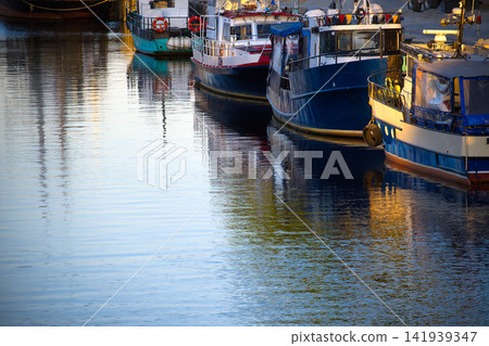 Colorful Fishing Boats Moored at Harbor Dock With Evening Reflections on Calm Water 141939347