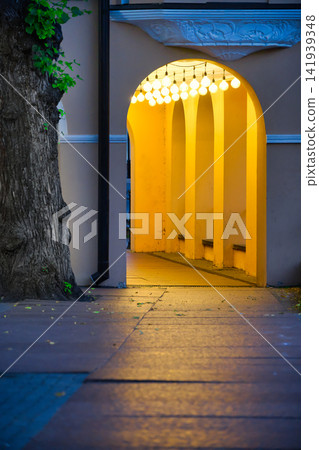 Warm yellow archway illuminated by string lights, with a large tree on the left Warm yellow archway illuminated by string lights, with a large tree on the left 141939348