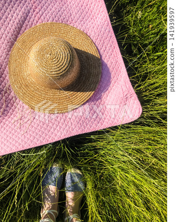 Summer flat lay. Picnic blanket, hat, woman legs on green grass. Summer flat lay. Picnic blanket, hat, woman legs on green grass. 141939597