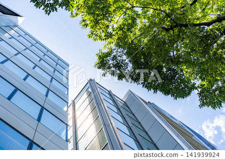 Green Building Modern Office Facade with Green Tree Canopy for Corporate ESG Sustainability and Eco Friendly Urban Real Estate Development, Low Angle Perspective Photo Green Building Modern Office Facade with Green Tree Canopy for Corporate ESG Sustainability and Eco Friendly Urban Real Estate Development, Low Angle Perspective Photo 141939924