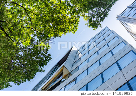 Green Building Modern Office Facade with Green Tree Canopy for Corporate ESG Sustainability and Eco Friendly Urban Real Estate Development, Low Angle Perspective Photo Green Building Modern Office Facade with Green Tree Canopy for Corporate ESG Sustainability and Eco Friendly Urban Real Estate Development, Low Angle Perspective Photo 141939925