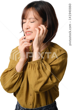 Asian woman with closed eyes touching face while wearing mustard blouse, expressing gentle discomfort in studio portrait Asian woman with closed eyes touching face while wearing mustard blouse, expressing gentle discomfort in studio portrait 141940860