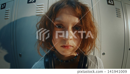 Teenage Girl With Headphones, Staring Directly in Camera, Stands Over School Lockers Teenage Girl With Headphones, Staring Directly in Camera, Stands Over School Lockers 141941009