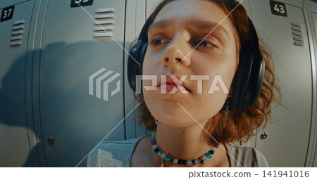 Young Girl in Headphones While Listening to Music in School Hallway 141941016