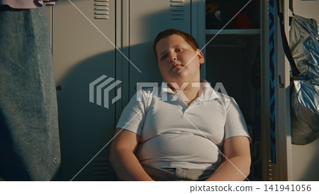Upset Primary School Boy Sitting Alone on Hallway Floor beside Open Locker in School Corridor Upset Primary School Boy Sitting Alone on Hallway Floor beside Open Locker in School Corridor 141941056