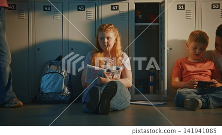 Elementary School Students Spending Free Time in Hallway, Sitting on Floor near Metal Lockers Elementary School Students Spending Free Time in Hallway, Sitting on Floor near Metal Lockers 141941085