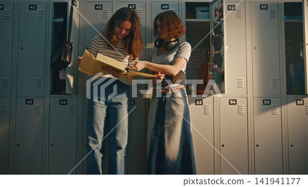 Two Teenage Girls Reviewing Homework Project by School Lockers Two Teenage Girls Reviewing Homework Project by School Lockers 141941177