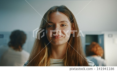 Cheerful Long Haired Teenage Girl Standing Near School Lockers and Smiling Cheerful Long Haired Teenage Girl Standing Near School Lockers and Smiling 141941186