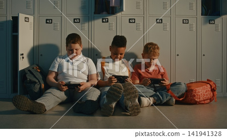 School Children Relax by Lockers While Sharing Content on Portable Devices Between Classes School Children Relax by Lockers While Sharing Content on Portable Devices Between Classes 141941328