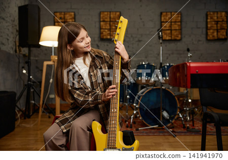 Young lady happily preparing her lively yellow electric guitar for performance Young lady happily preparing her lively yellow electric guitar for performance 141941970