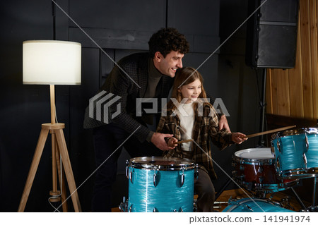 Mentor guides young girl through her drumming lesson in inviting studio setting Mentor guides young girl through her drumming lesson in inviting studio setting 141941974