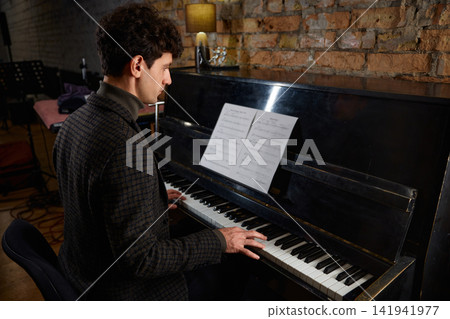 Man playing piano. Focused musician rehearsing with warm ambient lighting Man playing piano. Focused musician rehearsing with warm ambient lighting 141941977