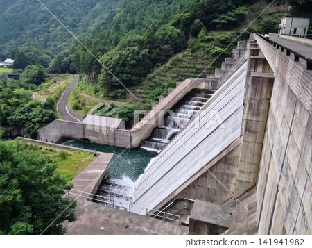 The dam's discharge facilities and the flowing water located in a lush, mountainous area. The dam's discharge facilities and the flowing water located in a lush, mountainous area. 141941982