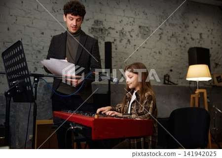 Girl musician dedicated to practicing her keyboard skills in softly illuminated studio Girl musician dedicated to practicing her keyboard skills in softly illuminated studio 141942025