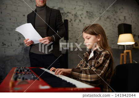 Girl musician dedicated to practicing her keyboard skills in softly illuminated space Girl musician dedicated to practicing her keyboard skills in softly illuminated space 141942044