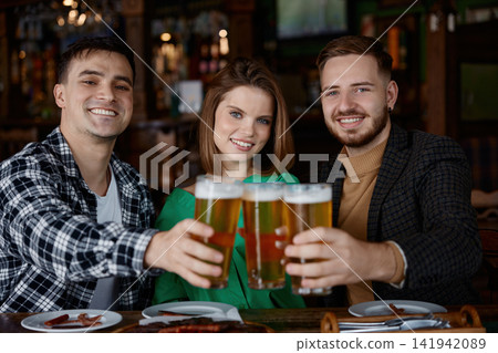 Friends cheering with beer glasses at cozy wooden pub table. Friends cheering with beer glasses at cozy wooden pub table. 141942089