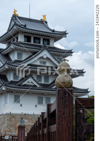 A historic Japanese castle and gourd decorations stand tall under a cloudy sky. A historic Japanese castle and gourd decorations stand tall under a cloudy sky. 141942226
