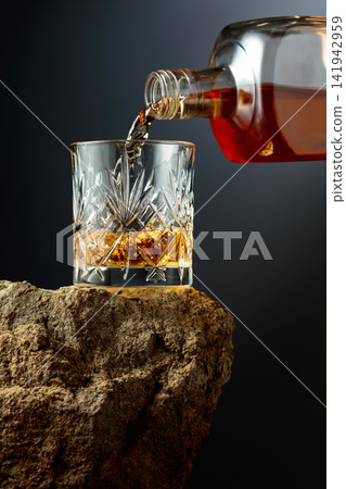 Whiskey is poured from a bottle into a glass. 141942959