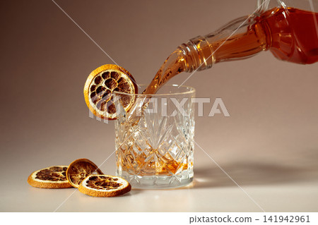 Whiskey is poured into a in crystal glass garnished with dried orange slices. Whiskey is poured into a in crystal glass garnished with dried orange slices. 141942961
