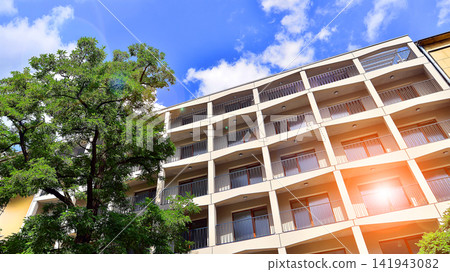 Modern residential building with new apartments in a green residential area. Eco architecture. Green tree and new apartment building. The harmony of nature and modernity. Modern residential building with new apartments in a green residential area. Eco architecture. Green tree and new apartment building. The harmony of nature and modernity. 141943082