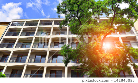 Modern residential building with new apartments in a green residential area. Eco architecture. Green tree and new apartment building. The harmony of nature and modernity. Modern residential building with new apartments in a green residential area. Eco architecture. Green tree and new apartment building. The harmony of nature and modernity. 141943083