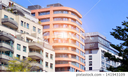 Modern residential building with new apartments in a green residential area. Eco architecture. Green tree and new apartment building. The harmony of nature and modernity. Modern residential building with new apartments in a green residential area. Eco architecture. Green tree and new apartment building. The harmony of nature and modernity. 141943109