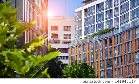 Modern residential building with new apartments in a green residential area. Eco architecture. Green tree and new apartment building. The harmony of nature and modernity. Modern residential building with new apartments in a green residential area. Eco architecture. Green tree and new apartment building. The harmony of nature and modernity. 141943117