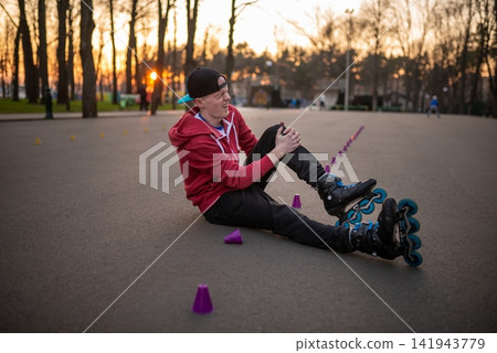 Injured rollerblader holding his knee after a fall on an asphalt track Injured rollerblader holding his knee after a fall on an asphalt track 141943779