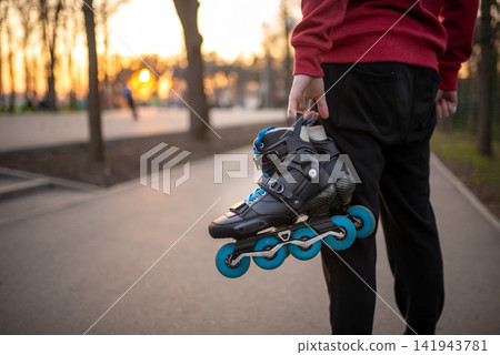Close up of a person holding a pair of black inline skates at sunset 141943781