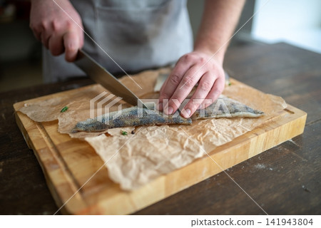 Cook slicing a seasoned raw fish fillet on a cutting board Cook slicing a seasoned raw fish fillet on a cutting board 141943804