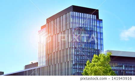 City life, urban landscape and ecology. Modern office complex with glass facades and smooth lines against backdrop of green trees, concept of modern architecture. Organically building into nature. City life, urban landscape and ecology. Modern office complex with glass facades and smooth lines against backdrop of green trees, concept of modern architecture. Organically building into nature. 141943916